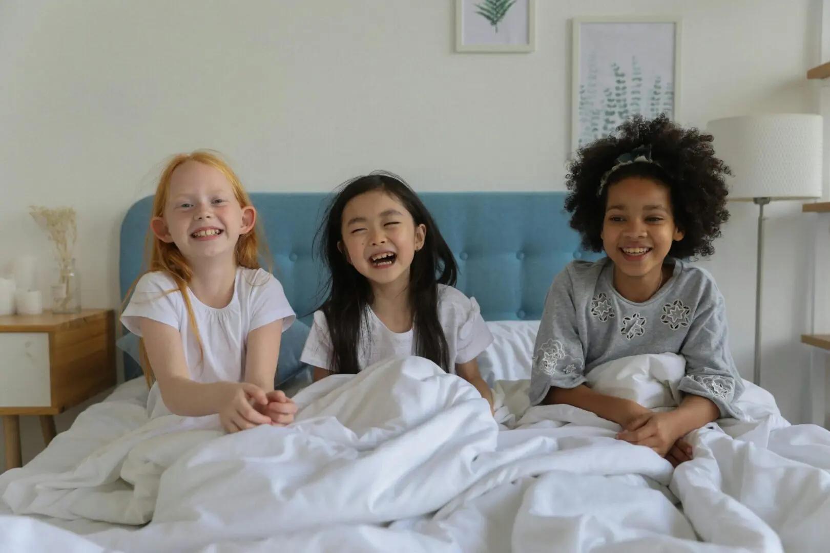 Three girls are sitting on a bed and smiling.